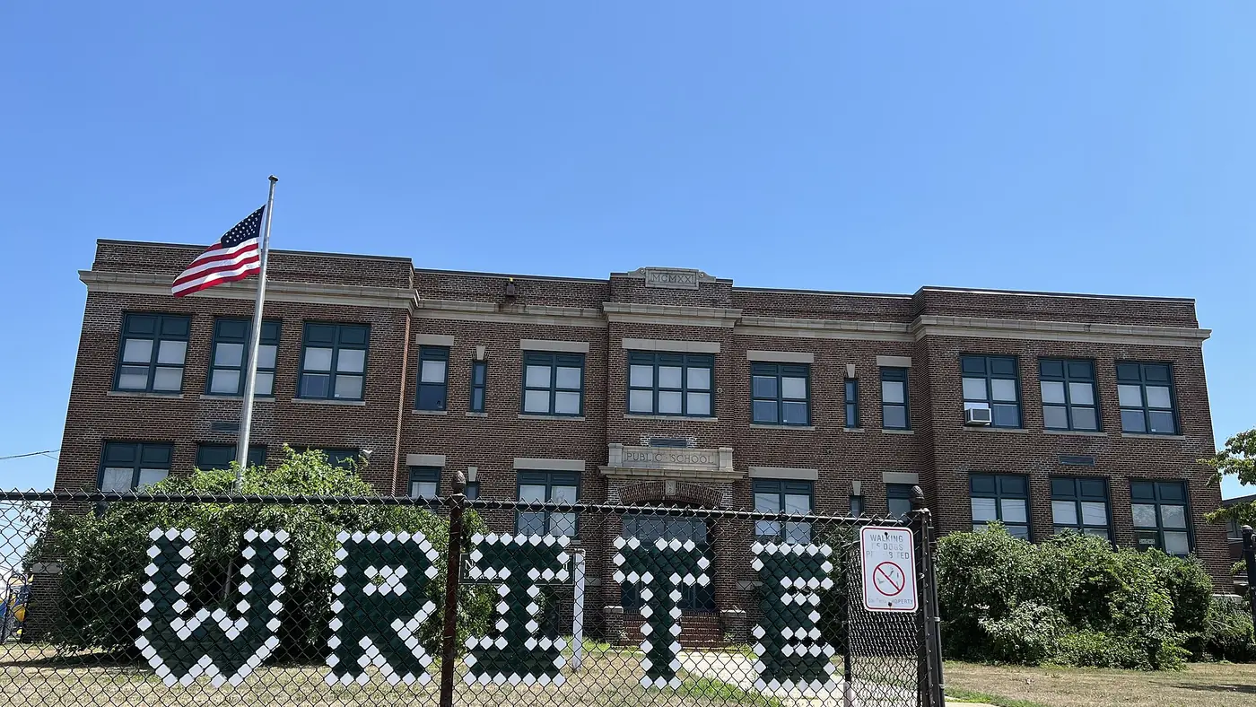 A brick public school building in Inwood behind a chain-link fence.